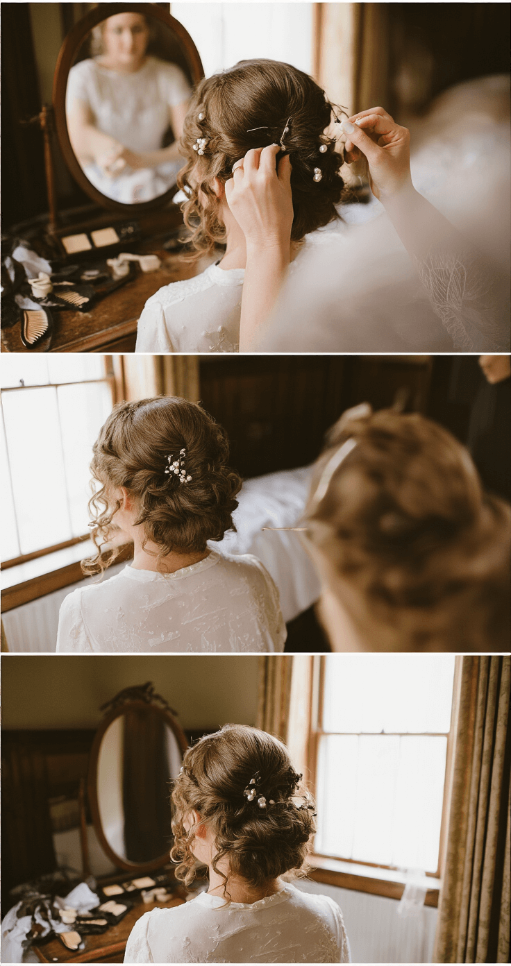 A bride in a Victorian-style bedroom prepares for her wedding, as pearl accessories are pinned into her curled hair. The antique mirror reflects warm morning light onto vintage styling tools and hair combs scattered around. The image captures various angles of the pearlescent pins glistening in the light, shot from above at a slight angle.