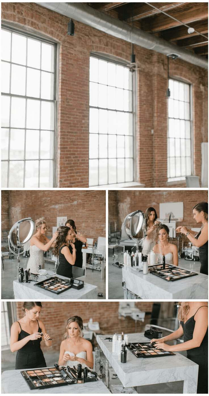 Bright bridal preparation space featuring exposed brick walls and factory windows, showcasing hands styling hair with modern tools and products at elegant marble stations, with a systematic professional kit visible and natural light enhanced by fill lights.