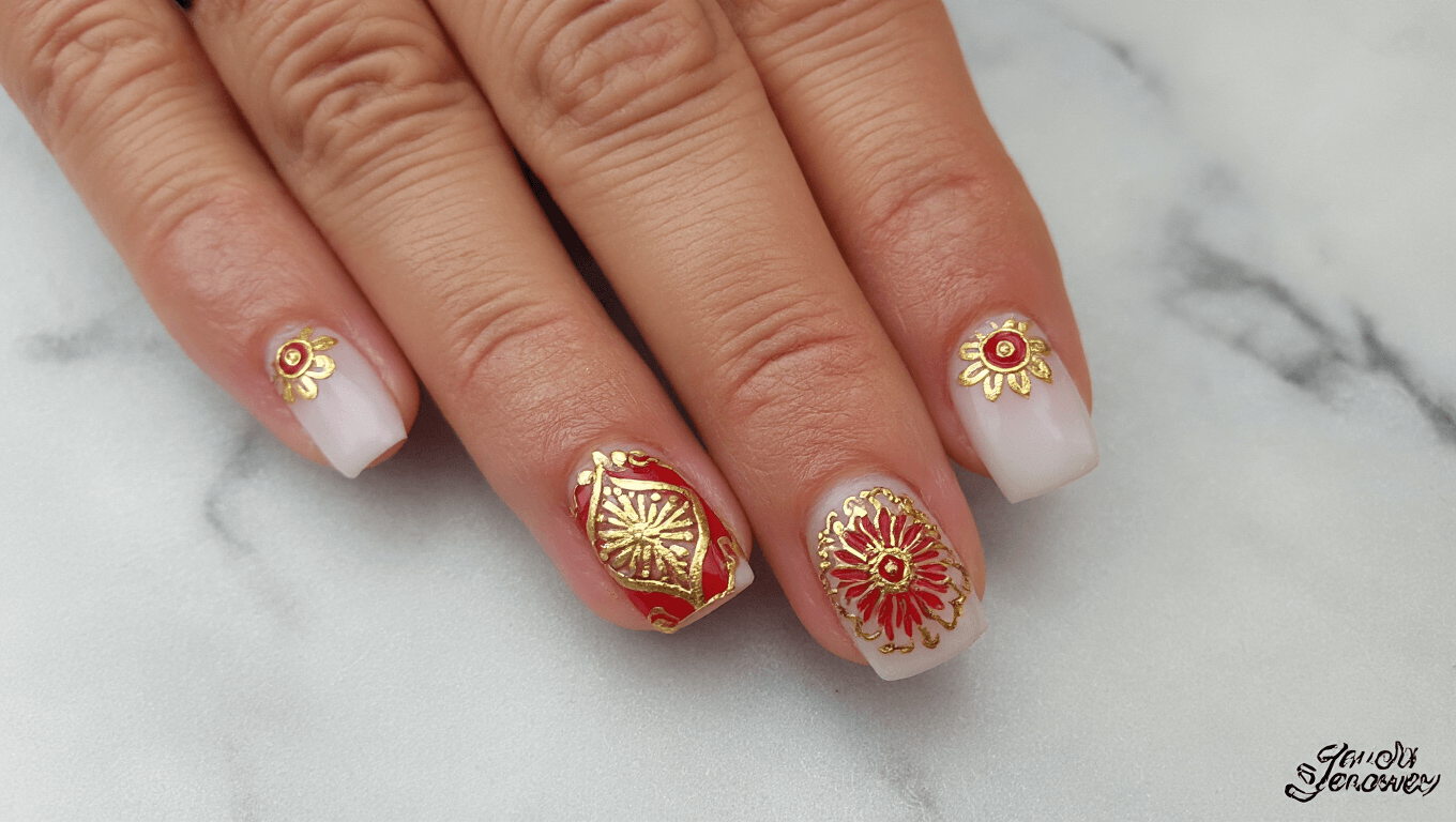 Bridal mandala nail art featuring red and gold accents on a marble background.